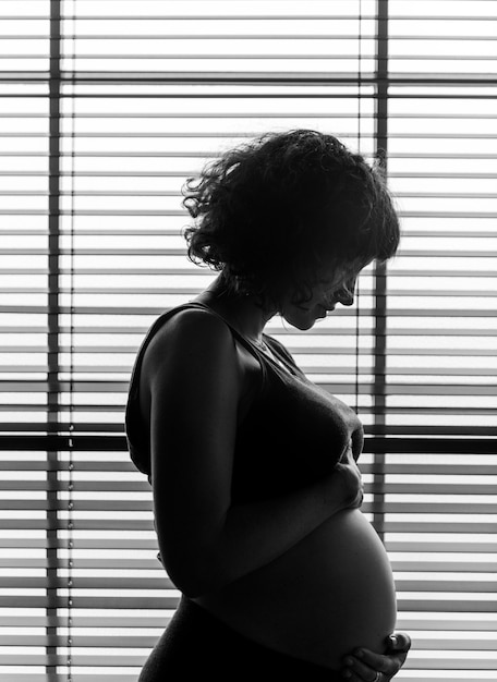 Беременная женщина, стоящая у окна
