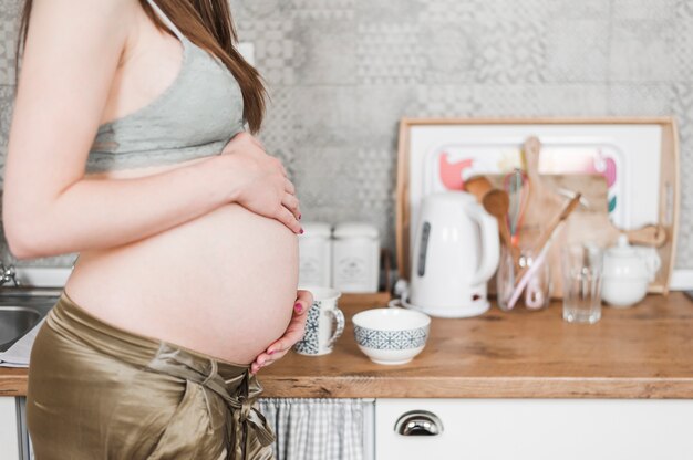 彼女の腹に触れる台所のカウンターの近くに立っている妊娠中の女性