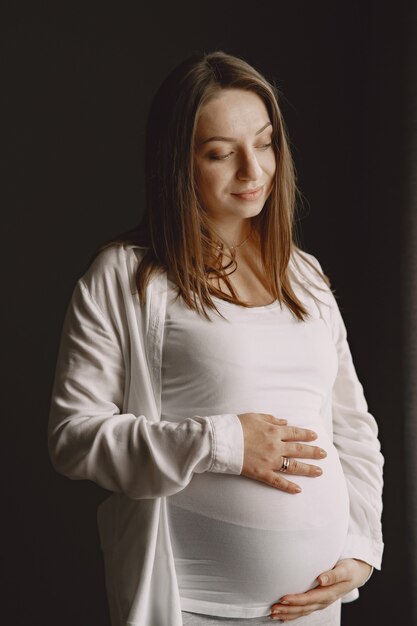 Pregnant woman standing and touching her belly.