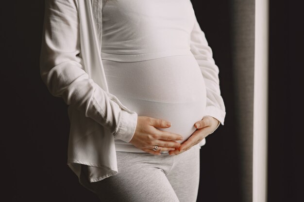 Pregnant woman standing and touching her belly.