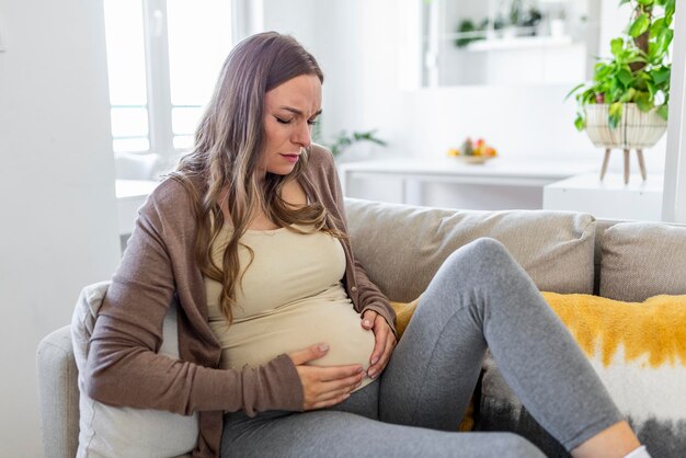 Pregnant woman suffering during her pregnancy, with back pain and headaches. pregnant woman sitting on the sofa holding her belly with worried face expression.