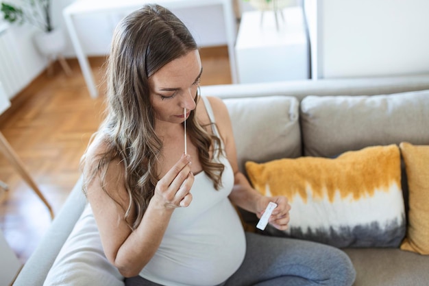 抗原キットを使用して自宅でcovid-19のセルフスワブホームテストを受けている妊婦。コロナウイルスの感染をチェックするための鼻スティックの紹介。検疫、パンデミック。