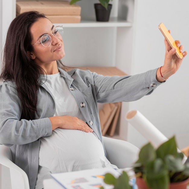 Pregnant woman taking selfie at home while working