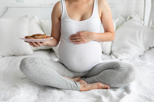 Беременная женщина, касаясь ее живот, держа тарелку с печеньем