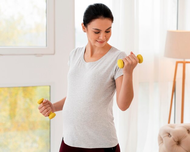 Беременная женщина тренируется с весами
