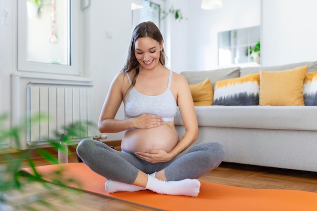 彼女の腹を愛撫するヨガを訓練している妊婦若い幸せな妊婦は、赤ちゃんのことを考えてリラックスし、彼女の将来の生活を楽しんでいます母性妊娠ヨガの概念