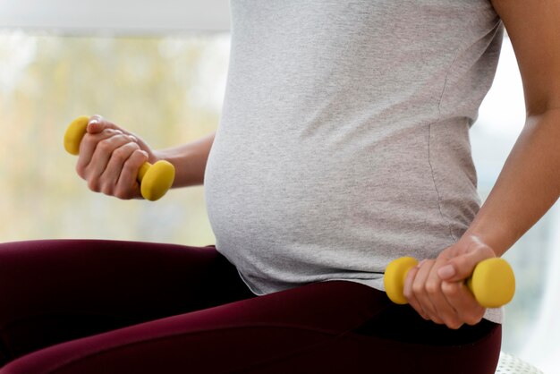 Pregnant woman using yellow weights close-up