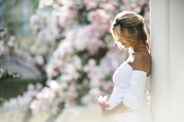 Pregnant woman in a white dress standing near the wall