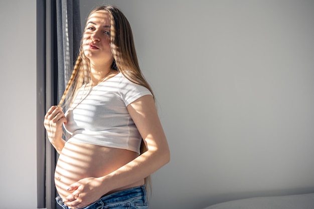 Free photo a pregnant woman at the window on a sunny morning