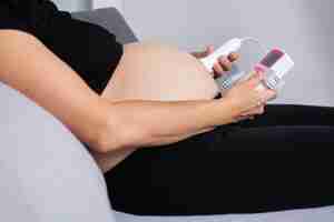 Бесплатное фото Беременная женщина с фетальным допплером слушает сердце ребенка сидя