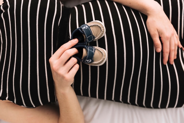 Free photo pregnant woman with baby shoes