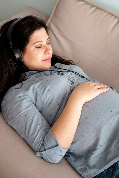 ソファの上に敷設のヘッドフォンで妊娠中の女性