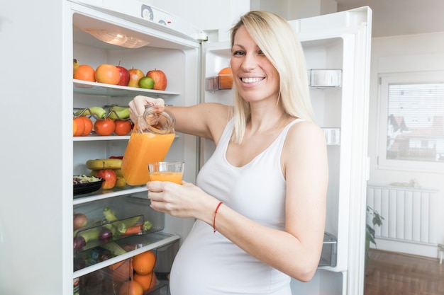 Free photo pregnant woman with juice from fridge