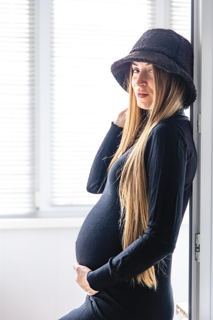 Free photo a pregnant woman with long hair in a black dress in the interior of the room