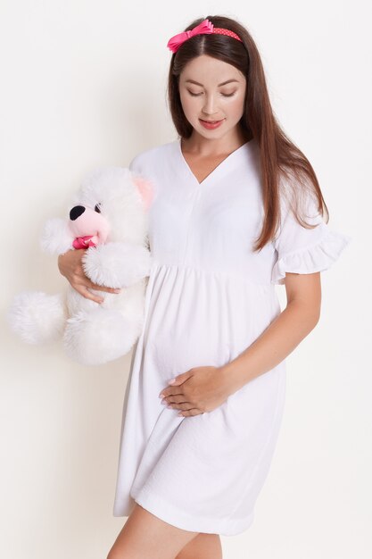 Pregnant woman with teddy bear wearing beautiful dress