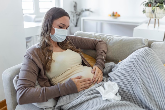 妊娠中​の​若い​成人​女性​が​自宅​の​ソファ​で​休んで​、​気分​が​悪い​。​若い​妊婦​は​フェイス​マスク付き​の​ソファ​に​座っている​covid​-​19​に​苦しんでいます​。​妊娠​の​症状