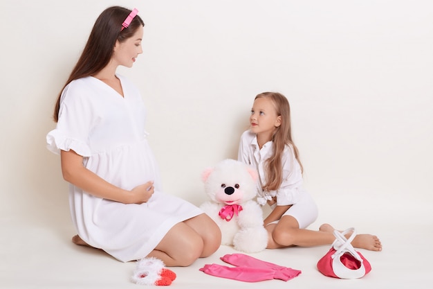 Pregnant young expectant mother playing with her daughter with bear