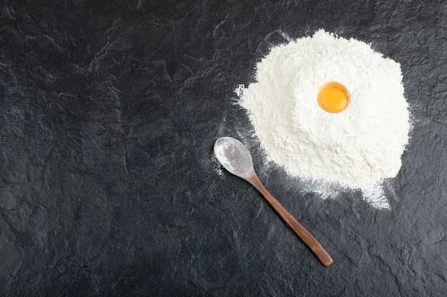 Preparation for bread with raw egg yolk and flour on black surface. 