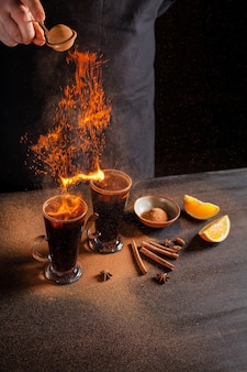 Preparation of mulled wine to serve, in a restaurant. mulled wine in the preparation of the chef's bar. the hands of the chef on a dark black background. burning mulled wine with sparks.