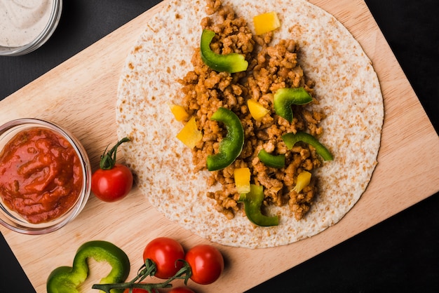 Preparation of taco on cutting board near tomatoes and sauce 