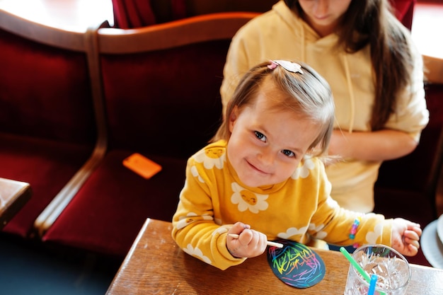 Free photo preparing to easter concept baby girl with mother drawing on egg