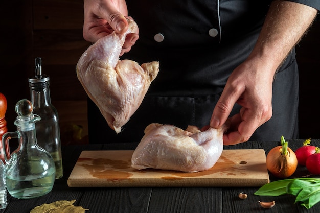 Подготовка к приготовлению куриных ножек на кухне ресторана шеф-повар или повар держит сырую куриную ножку