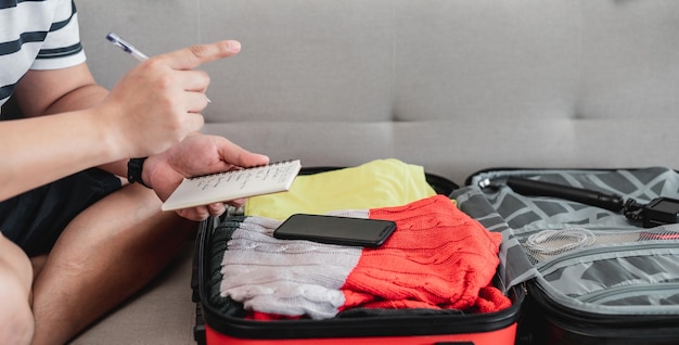 夏休み旅行のためのスーツケースの準備若い男が荷物の中のアクセサリーやものをチェックする旅行休暇と休暇のコンセプト