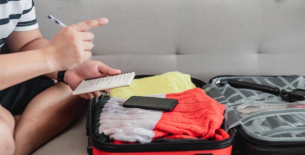 Preparing suitcase for summer vacation trip Young man checking accessories and stuff in luggage Travel holiday and vacation concept