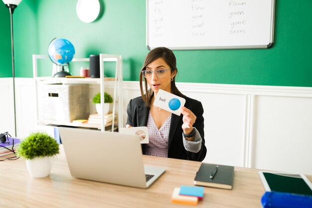 Preschool teacher holding educational cards and teaching online the english vocabulary to her kindergarten students