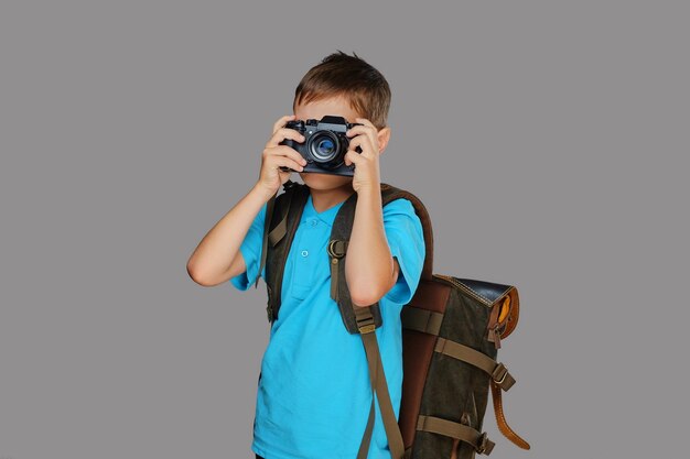 Мальчик-дошкольник фотографирует профессиональным фотоаппаратом. Изолированные на сером фоне.