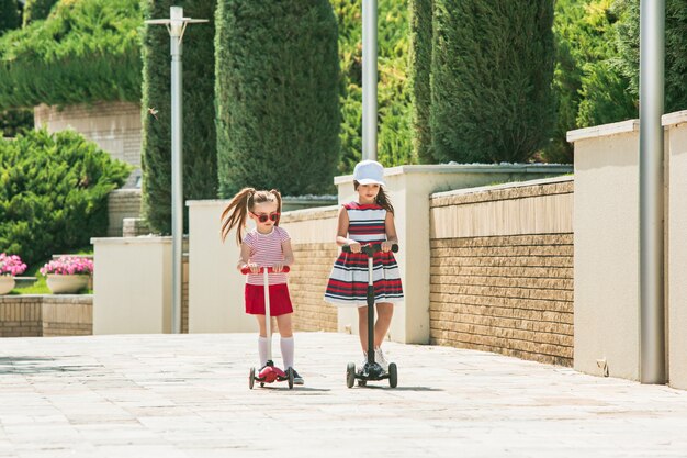 Preschooler girls riding scooter outdoors.