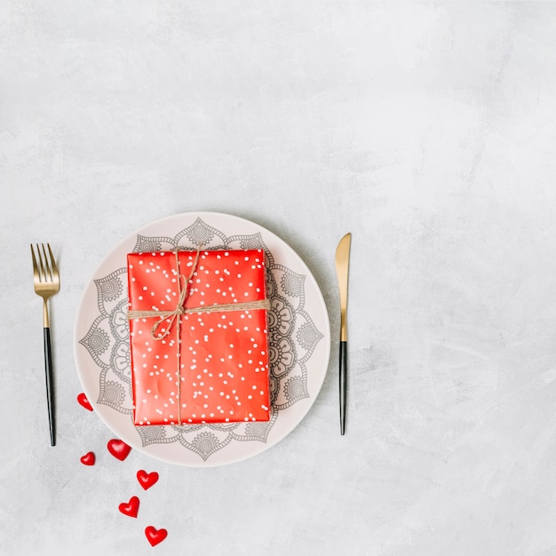 Present box on plate near cutlery and ornament hearts