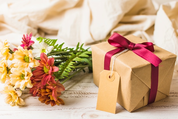 Present box with brown tag and flower bunch on table