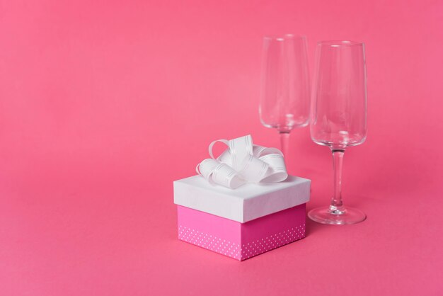 Подарочная коробка с пустым бокалом шампанского на розовом фоне
