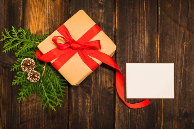 Present box with red bow near coniferous branch and paper 