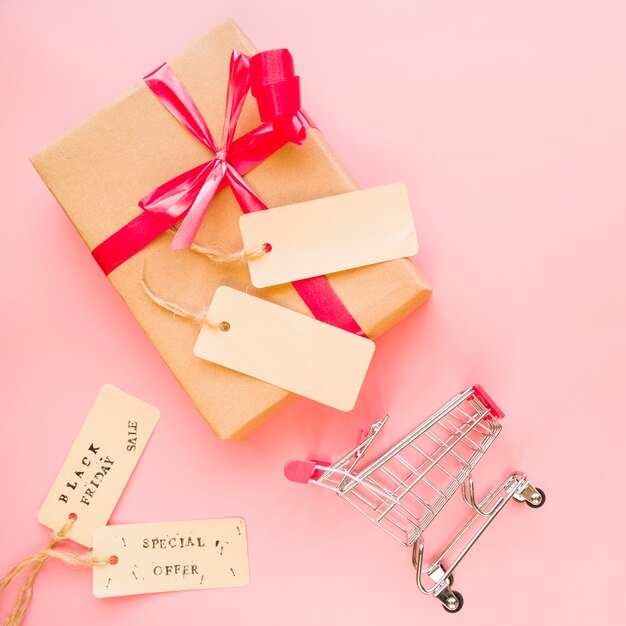 Present box with red bow near shopping trolley and sale labels