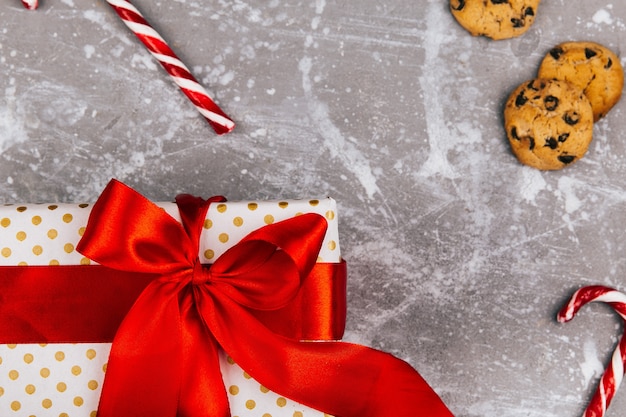 Present box with red ribbon lies on grey floor with Christmas cookies, gingerbreads and red white candies