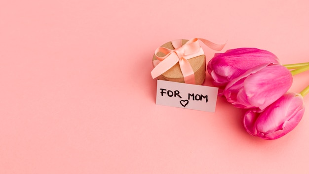 Present box with ribbon near note and flowers