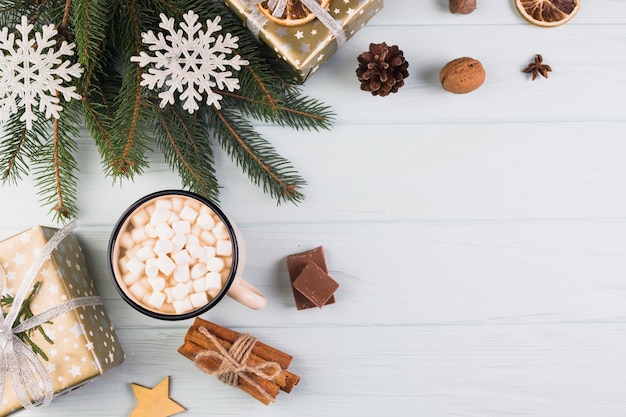 Present boxes in Christmas wrap near cup with marshmallows and fir branch