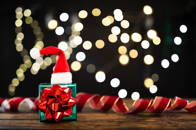 Present and Christmas hat near ribbon and garland lights