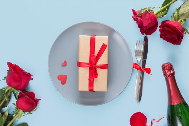 Present on plate near cutlery, roses and bottle of champagne 