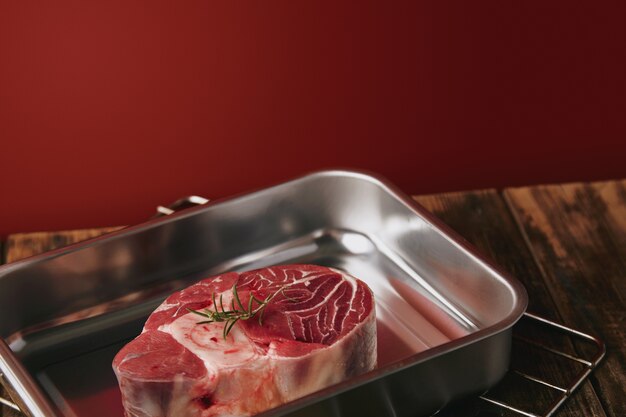 Presentetion of raw angus leg steak in silver steel pan on wooden table red background
