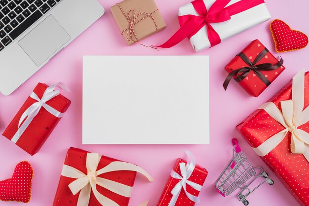 Presents and shopping trolley near paper sheet and laptop