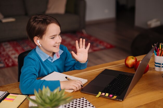 プレティーンの男の子がラップトップを使用してオンラインクラスを作成し、先生に挨拶します