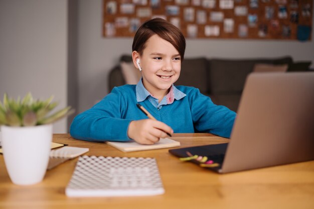 10 대 초반 소년이 노트북을 사용하여 선생님과 화상 통화, 온라인 수업, 메모 작성