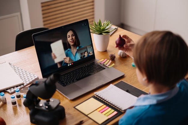 Free photo a preteen boy uses a laptop to make a video call with his teacher