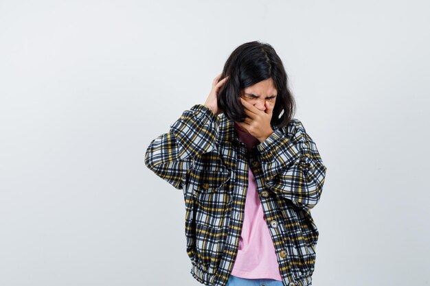 Preteen girl holding hand on mouth while yawning in shirt,jacket and looking tired , front view.