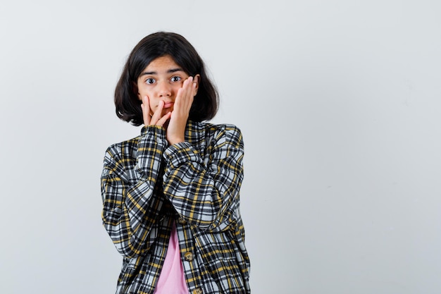 Ragazza preteen che si tiene per mano sulle guance in camicia, giacca e sembra eccitata. vista frontale.