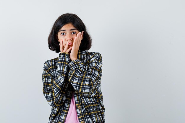 Preteen girl holding hands on cheeks in shirt,jacket and looking excited. front view.