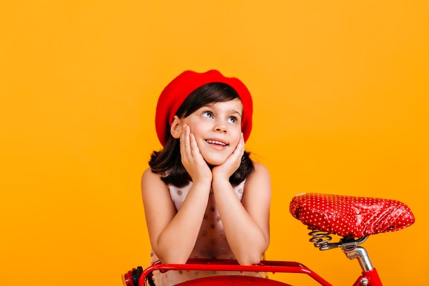 Preteen girl in red beret posing with bicycle.  brunette child isolated on yellow.